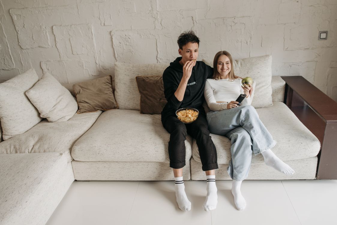 Couple relaxing on a couch with snacks while watching TV